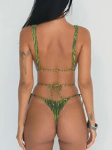 Back view of a woman wearing a green patterned one-piece swimsuit with a low back and string bikini bottom