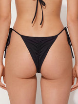 Rear view of black thong bikini bottom with adjustable side ties and ruched detailing
