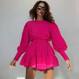Woman wearing a bright pink long-sleeved mini dress with puff sleeves and a tiered skirt, posing against a light background.