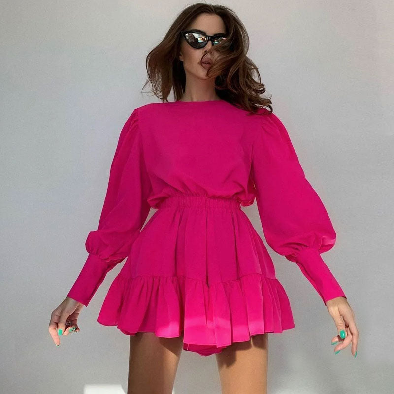 Woman wearing a bright pink long-sleeved mini dress with puff sleeves and a tiered skirt, posing against a light background.
