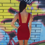 Back view of a woman wearing a red ruched bodycon dress with a low back, standing in front of a graffiti wall.
