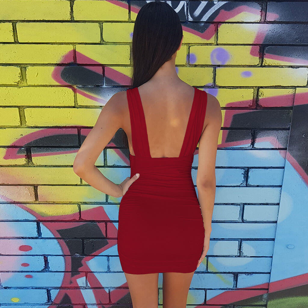 Back view of a woman wearing a red ruched bodycon dress with a low back, standing in front of a graffiti wall.