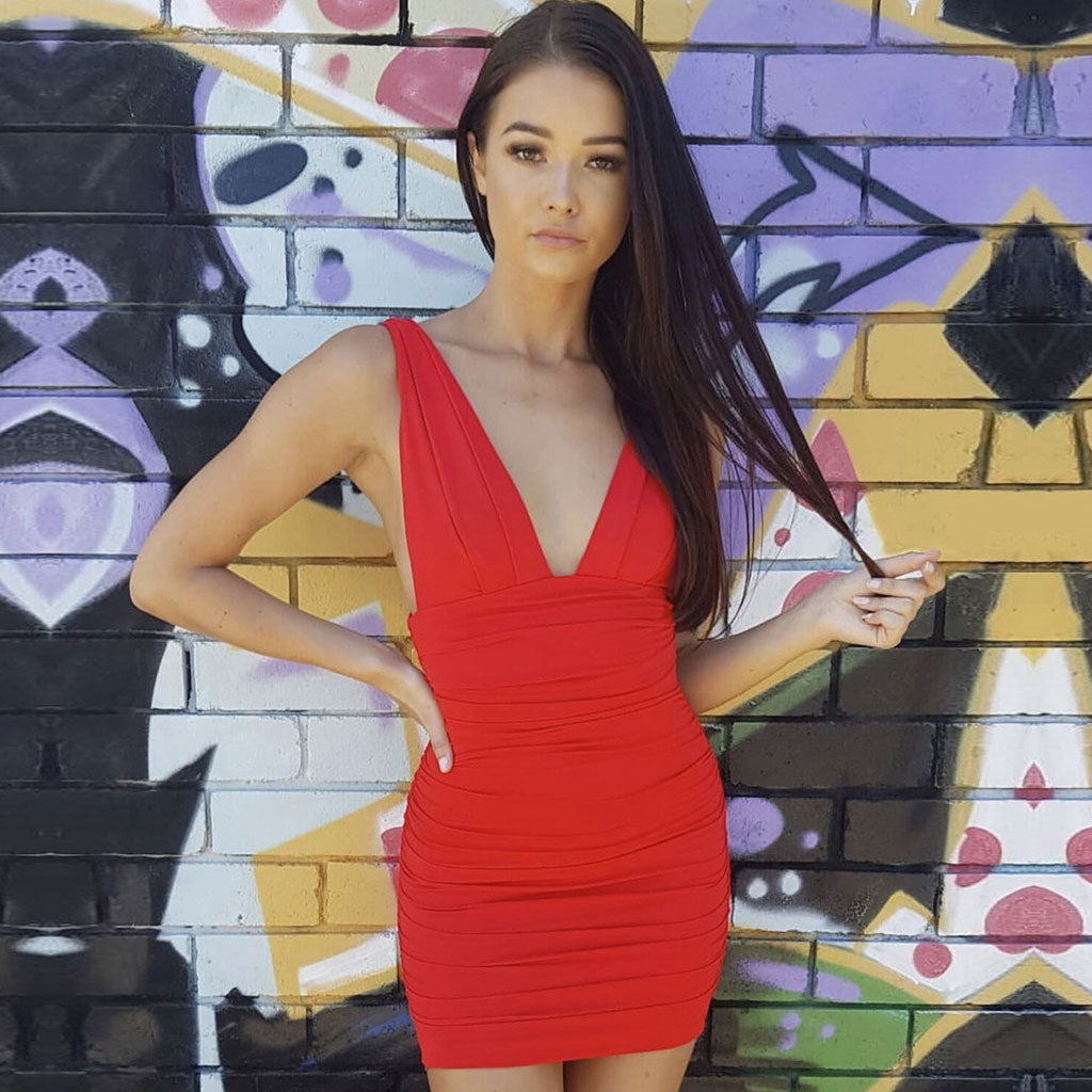 Woman wearing a red ruched V-neck mini dress standing in front of a graffiti wall.