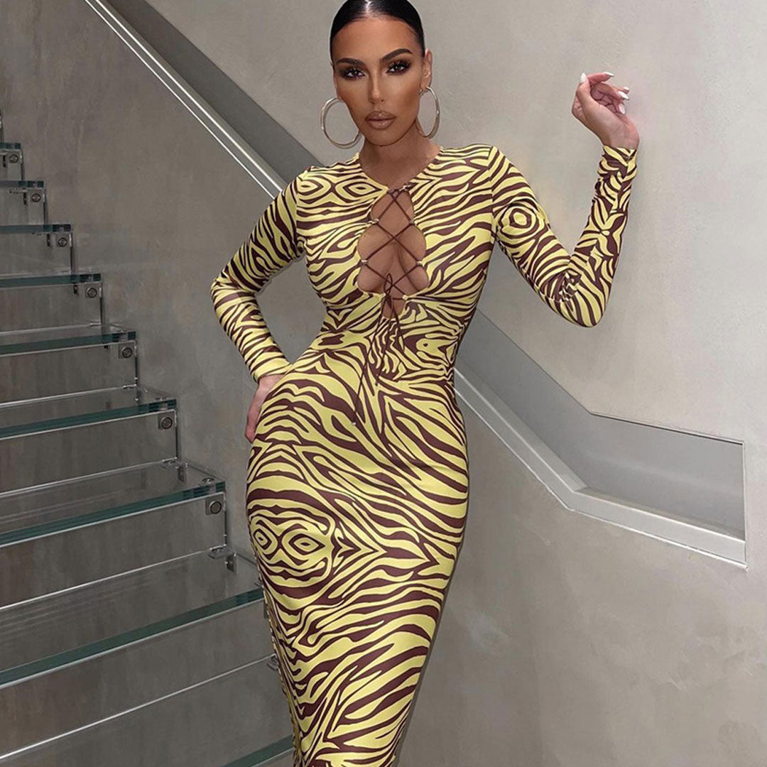 Woman wearing a yellow and brown zebra print midi dress with a lace-up neckline and long sleeves, standing on a modern staircase.