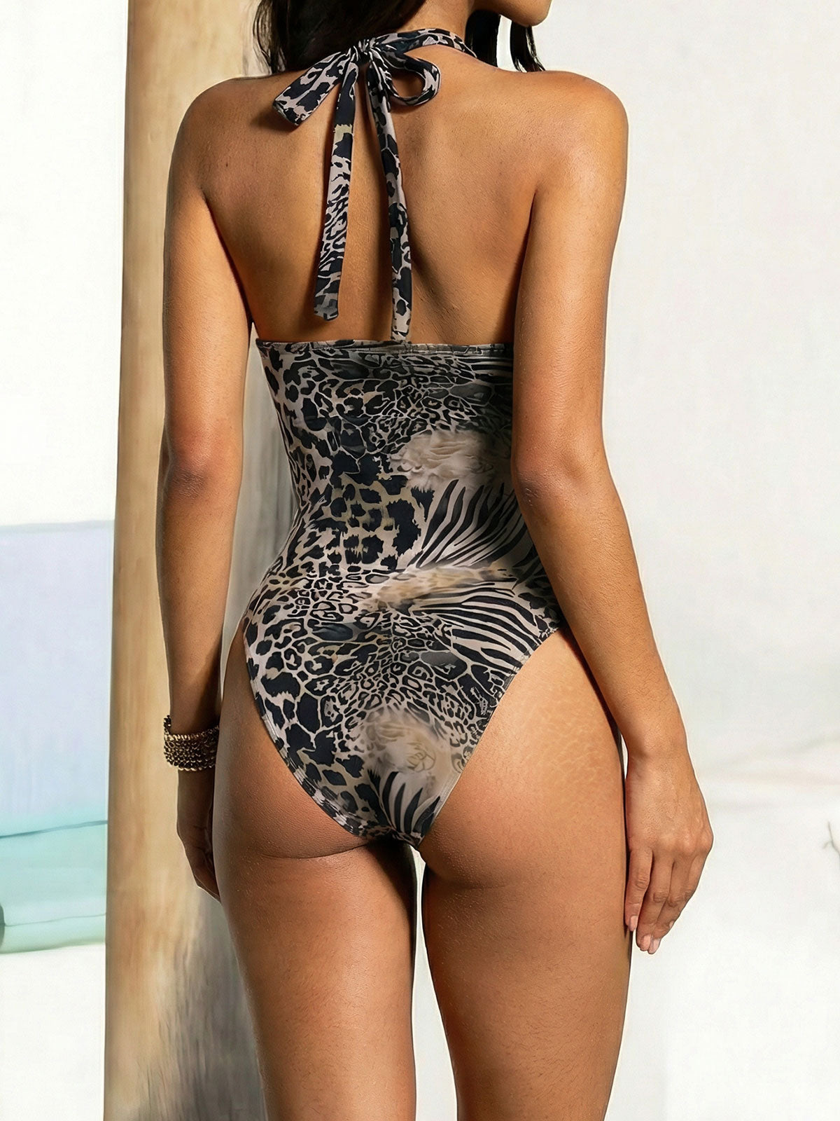 Back view of a woman in a one-piece swimsuit with a leopard and zebra print, showing the tie closure at the neck.