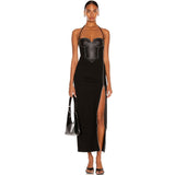 Full-length studio shot of a woman wearing a black halter dress with a corset bodice and thigh-high slit, holding a black handbag.