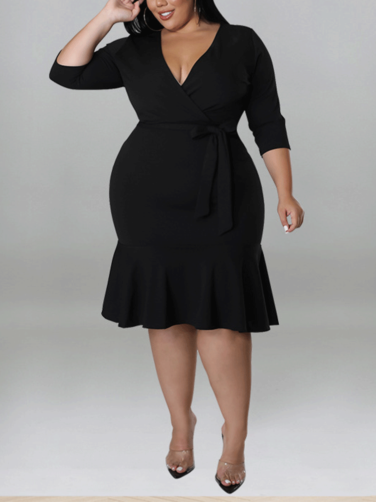 Plus-size model wearing a black wrap dress with a ruffle hem and three-quarter sleeves.