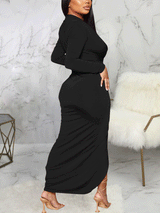 Side view of a woman in a black long-sleeved ruched maxi dress with a high slit, showcasing the fitted silhouette.