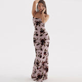 Woman wearing a long, light pink floral print dress with spaghetti straps and an open back.