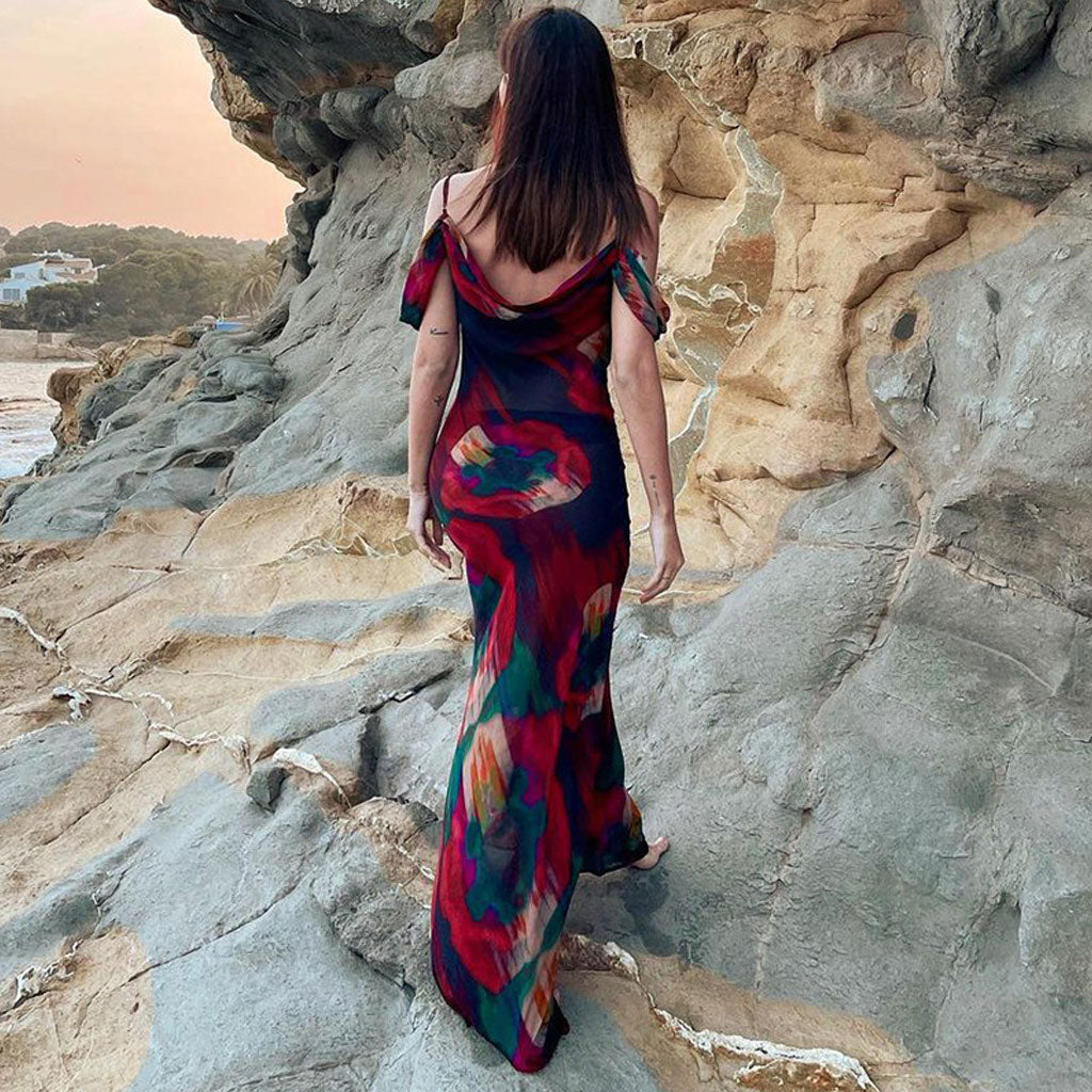 Rear view of a woman in a maxi dress with an abstract floral print, walking on rocky terrain.