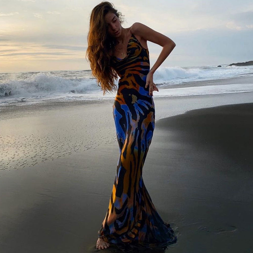 Woman wearing a flowing maxi dress with an abstract animal print on a beach at sunset.