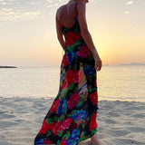 Woman in a black floral print maxi slip dress standing on a beach at sunset.