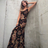 woman wearing a black floral print maxi dress leaning against a concrete wall