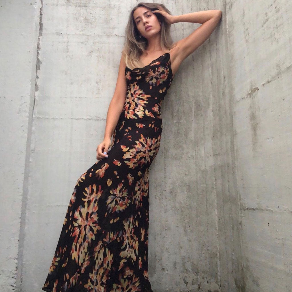 woman wearing a black floral print maxi dress leaning against a concrete wall