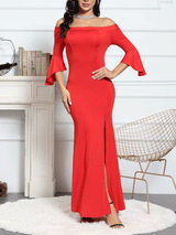 Woman wearing a red off-the-shoulder mermaid gown with bell sleeves and a high slit, standing in a room with a fireplace and chair.