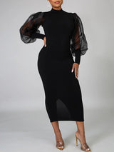 Rear view of a woman in a black midi dress featuring a back slit and sheer sleeves.