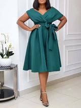 Woman posing with hands on hips, wearing a dark green A-line midi dress.